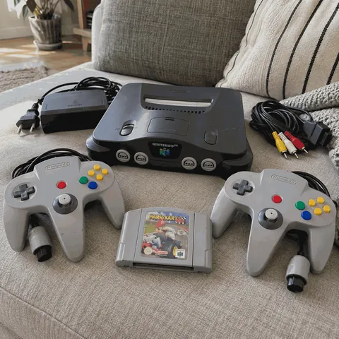 Consola Nintendo 64 con dos mandos y el cartucho de Mario Kart 64 sobre un sofá